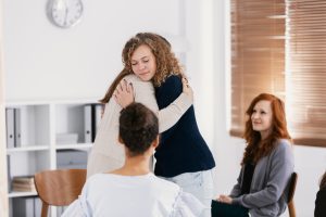 Two woman embracing each other in comfort during group therapy session.