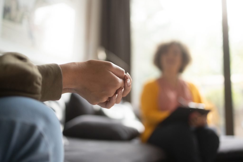 Close-up photo of a teenage girl's hands crossed. She is in a therapy session with her psychotherapist.