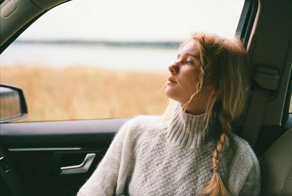 Somber young woman sitting in the passenger seat of a parked car, looking out the window.
